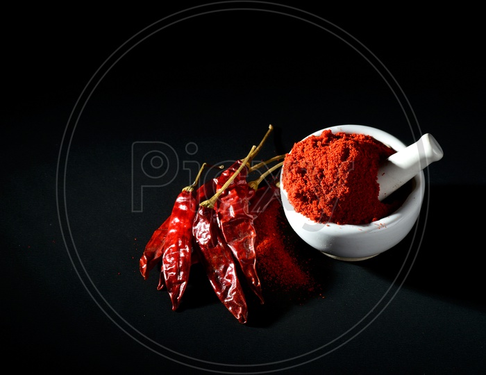 Red Chilli pepper powder in pestle with mortar and clay pot with Red Chilli Peppers on black background
