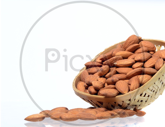 Almonds Or Badam Nuts In a Wooden Weaved  Bowl With a Heap On an Isolated White background