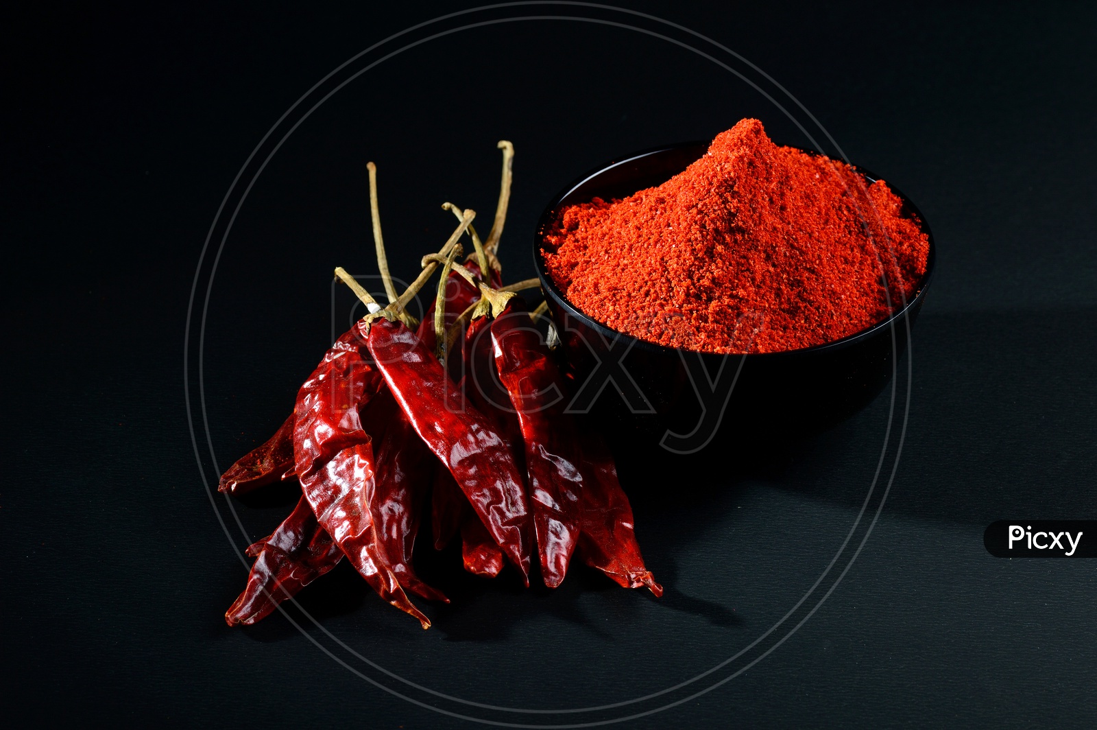 chilly powder in black bowl with red chilly, dried chillies on black background