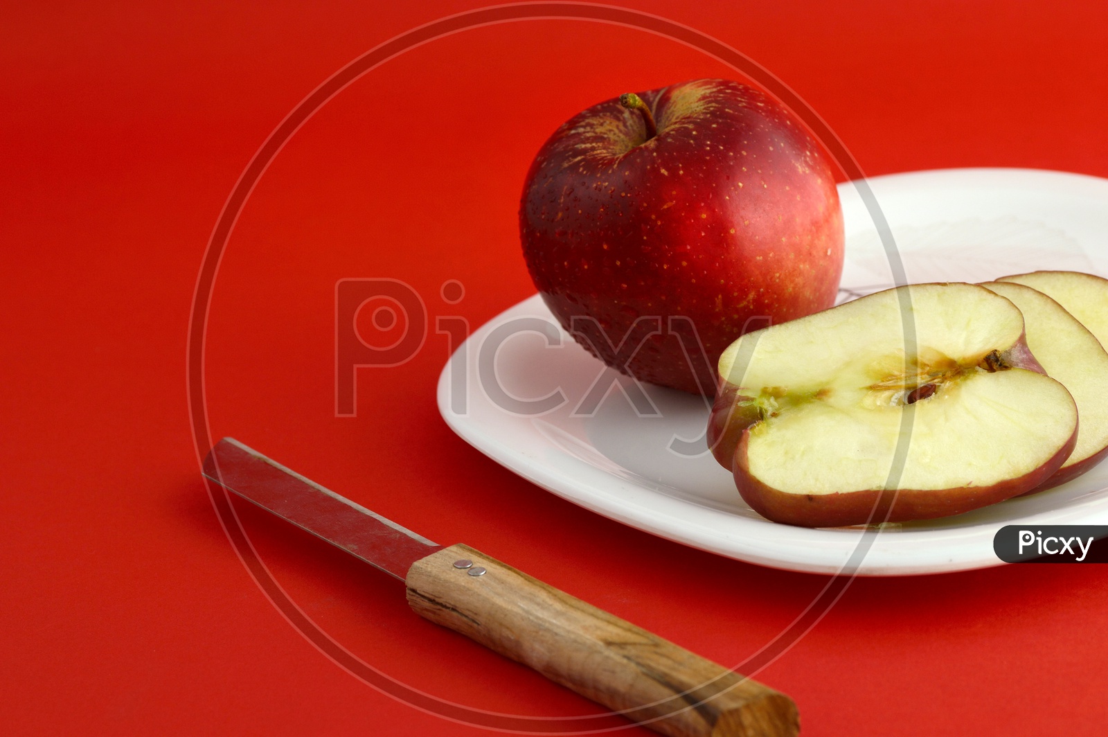 Ripen Red Apple Slices On White Plate With Knife  Over an Isolated Red Background