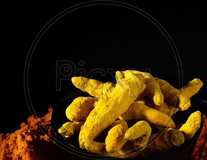 Turmeric powder and roots or barks on black background