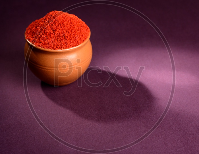 Red Chili Pepper powder in clay pot on dark background