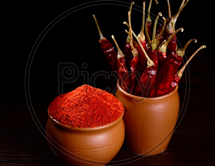 chilly powder with red chilly in clay pots, dried chillies on dark background