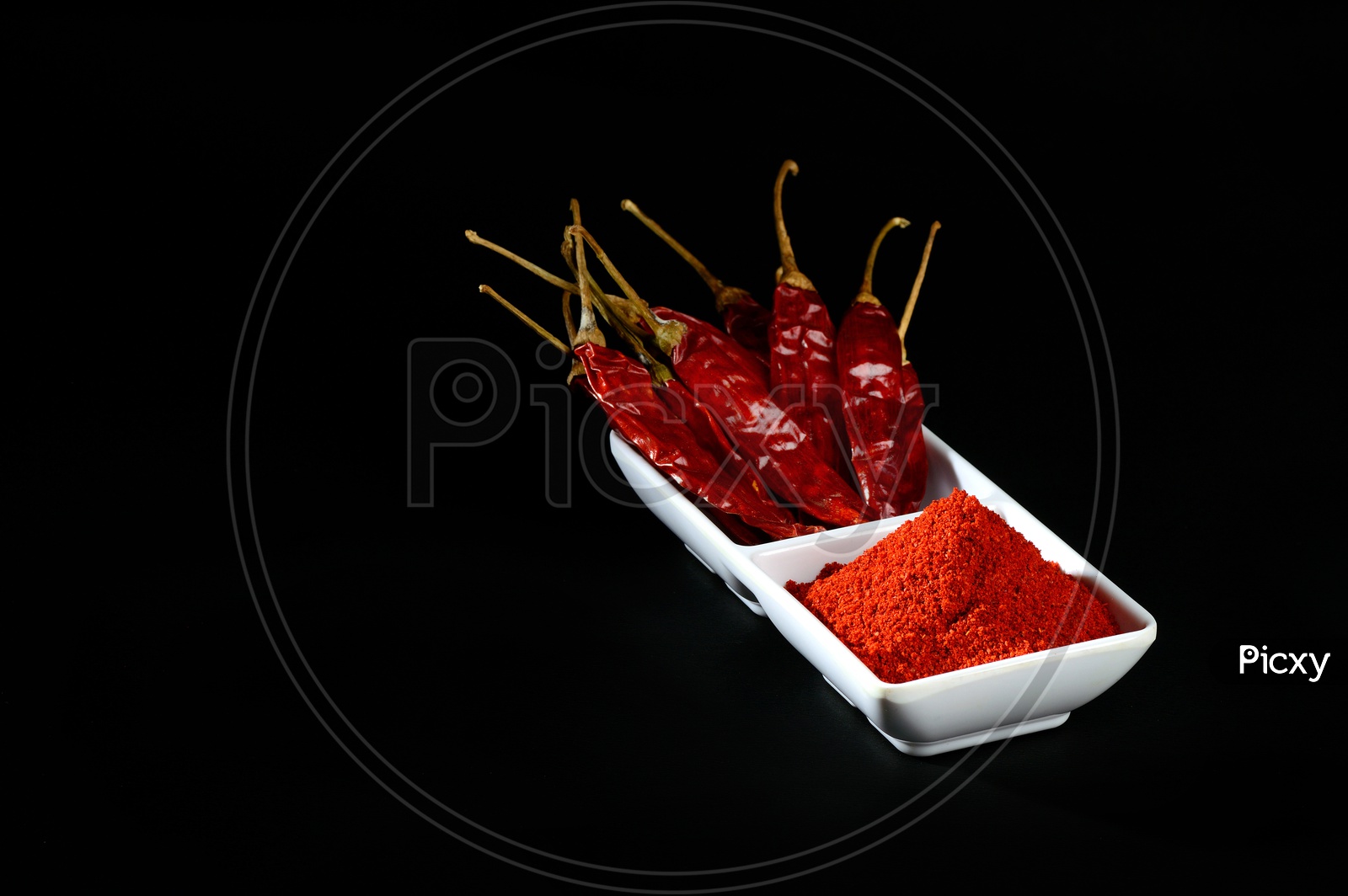 chilly powder with red chilly in white plate, dried chillies on black background