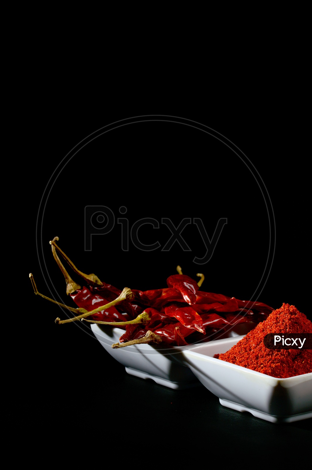 chilly powder with red chilly in white plate, dried chillies on black background