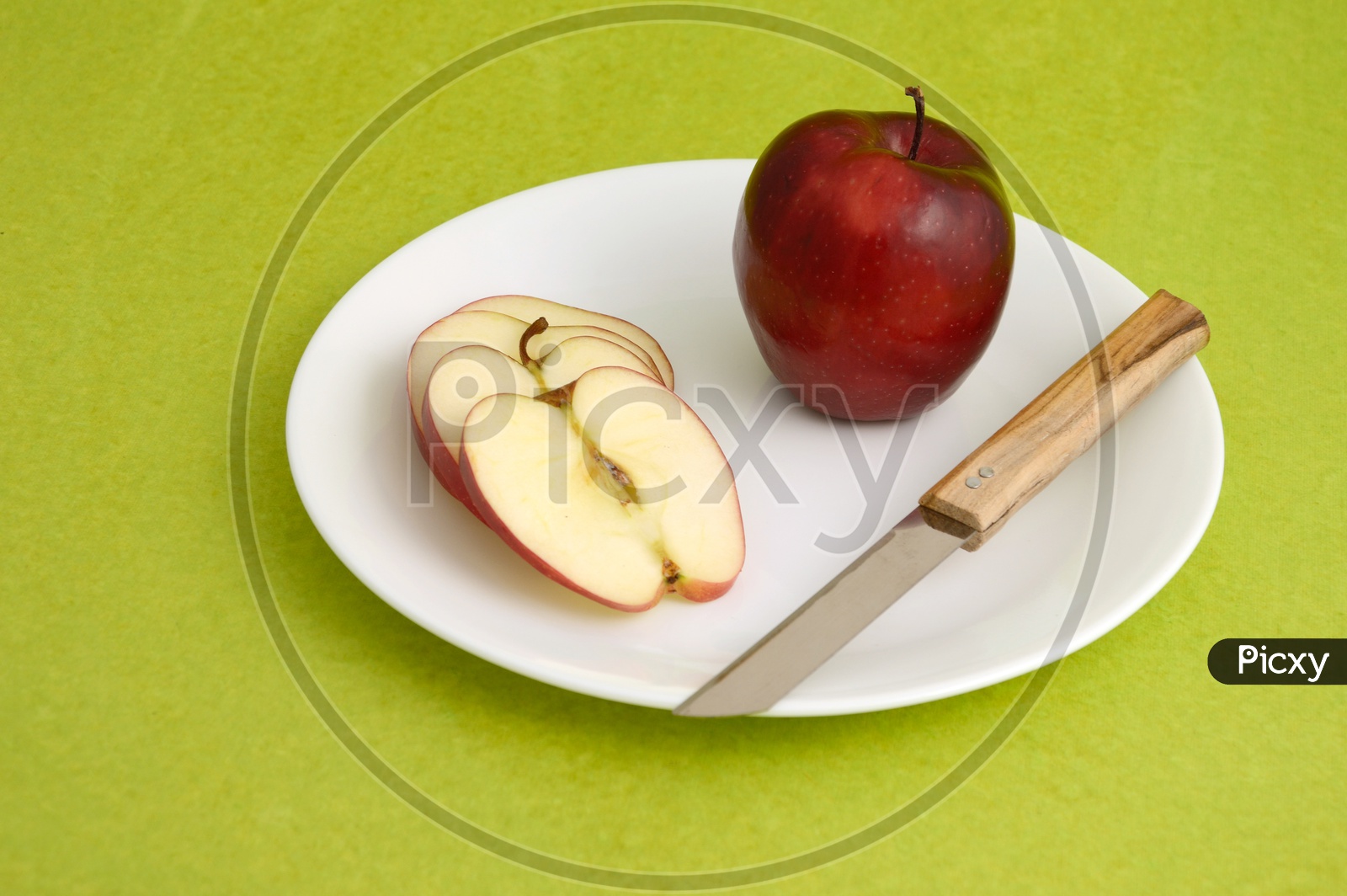 Fresh Red Apple Slices on White Plate With Fork and Knife On an Isolated Green  Background