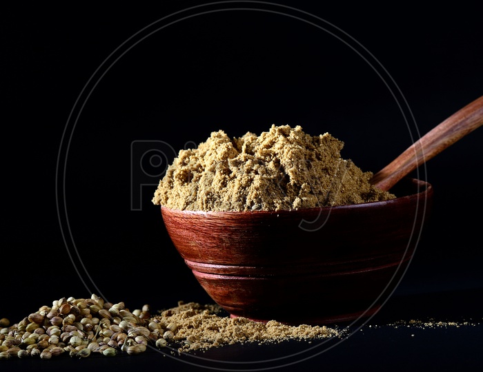 Coriander Powder in wooden bowl with seeds on black background