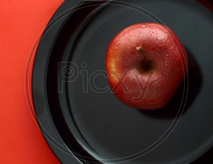 Ripen Red Apple on Black Plate With Knife And Fork Over an Isolated Red Background