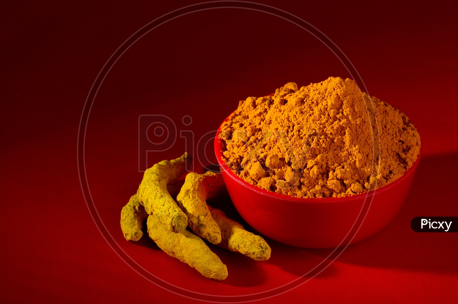 Dry Turmeric powder and roots or barks in red bowl on red background