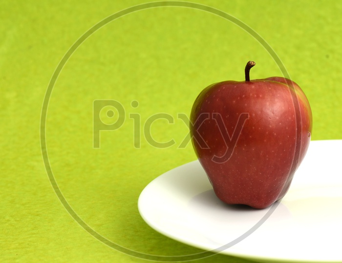 Fresh Red Apple On a  White Plate Over An Isolated Green Background