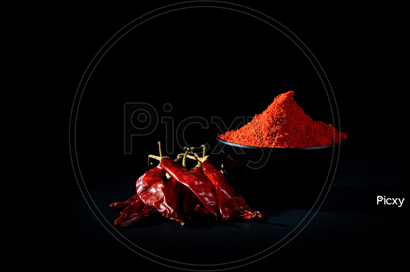 chilly powder in black bowl with red chilly, dried chillies on black background