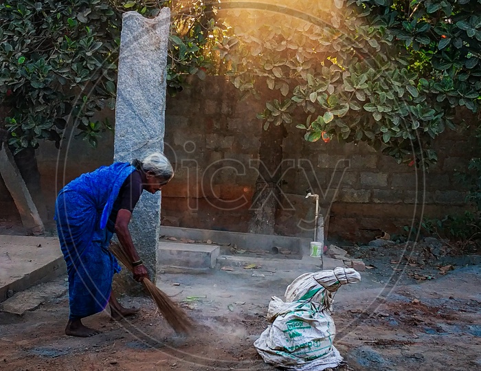 Old women sweeping the floor in front of her home