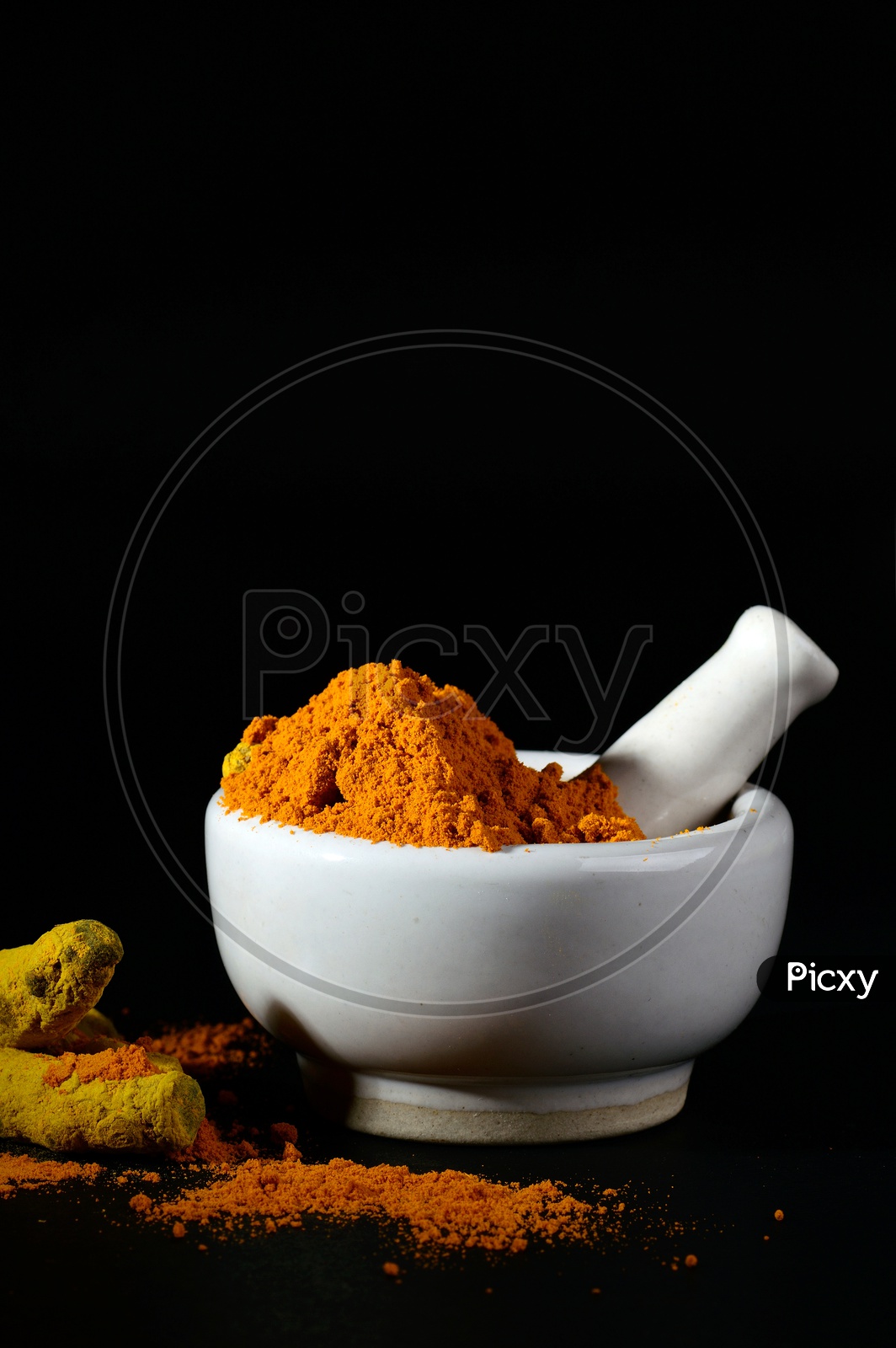 Turmeric powder in mortar with pestle and roots or barks on black background