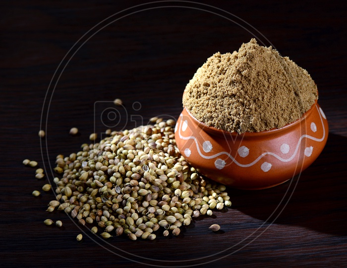 Coriander seeds and Powdered coriander in clay pot on wooden background.