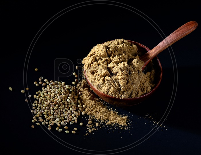 Coriander Powder in wooden bowl with seeds on black background