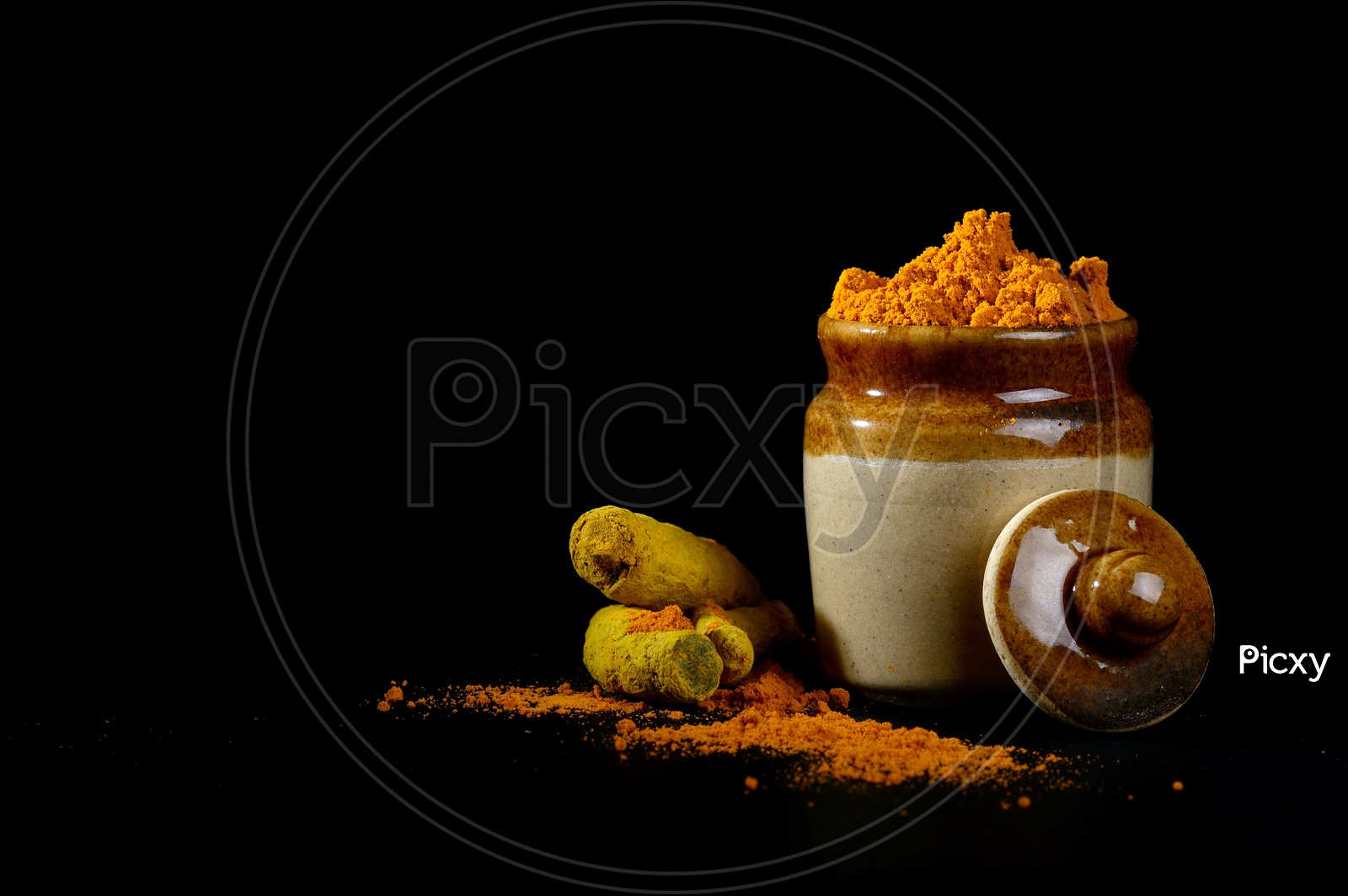 Turmeric powder in clay pot with roots or barks on black background