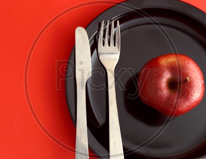 Ripen Red Apple on Black Plate With Knife And Fork Over an Isolated Red Background