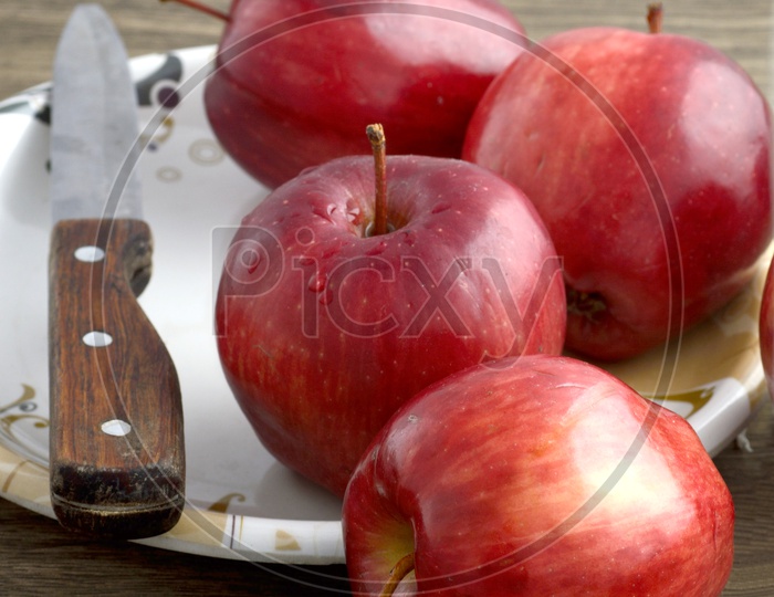 Ripen Red Apples With Knife   On a  Plate Over an Isolated  Wooden Background