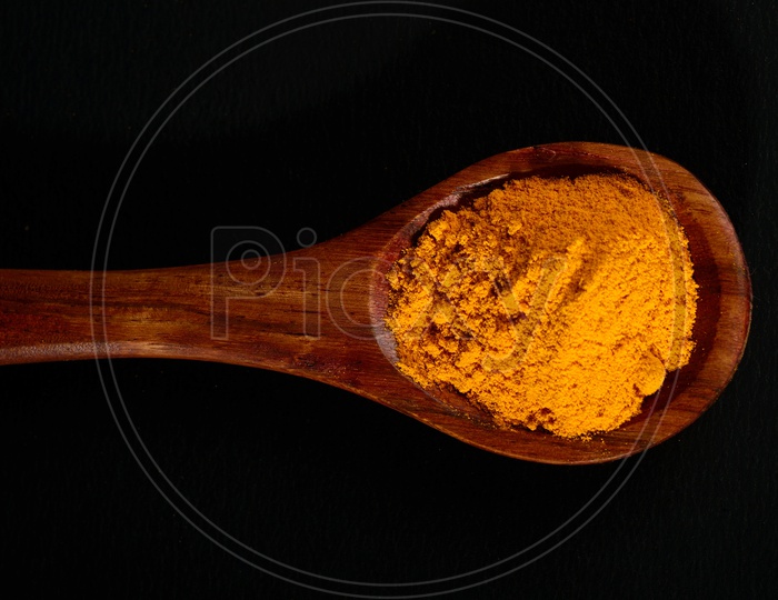 Turmeric powder in spoon on black background