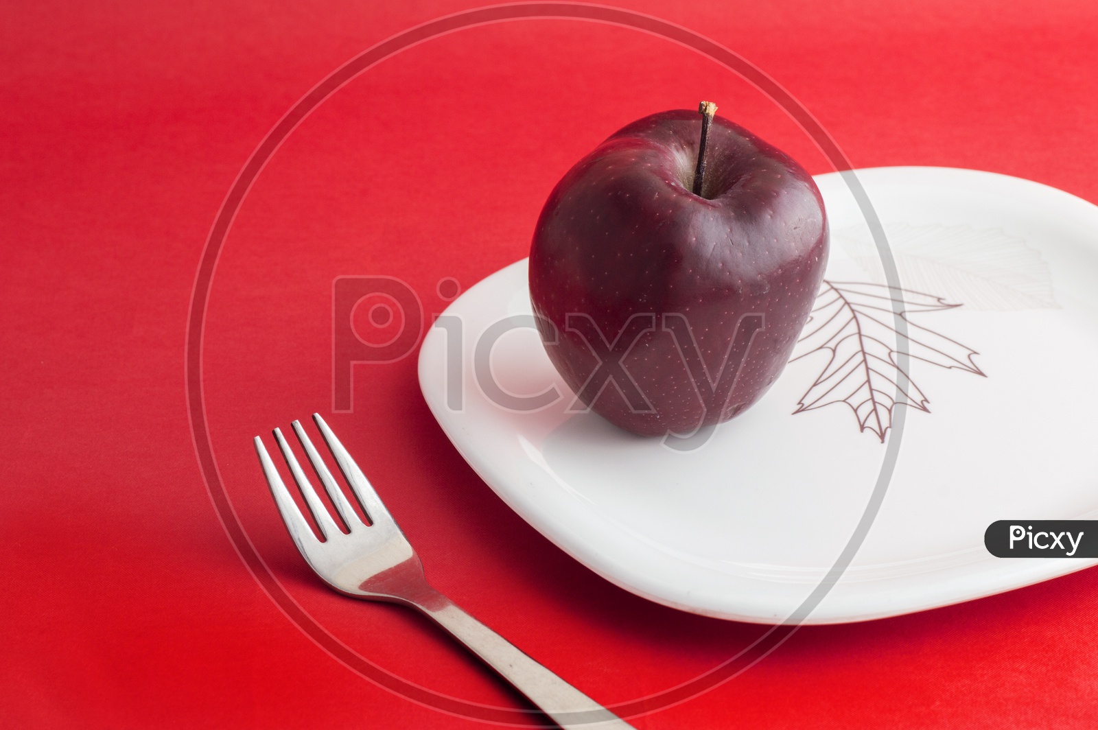 A Ripen Red Apple On White Plate With Fork  on an Isolated Red Background