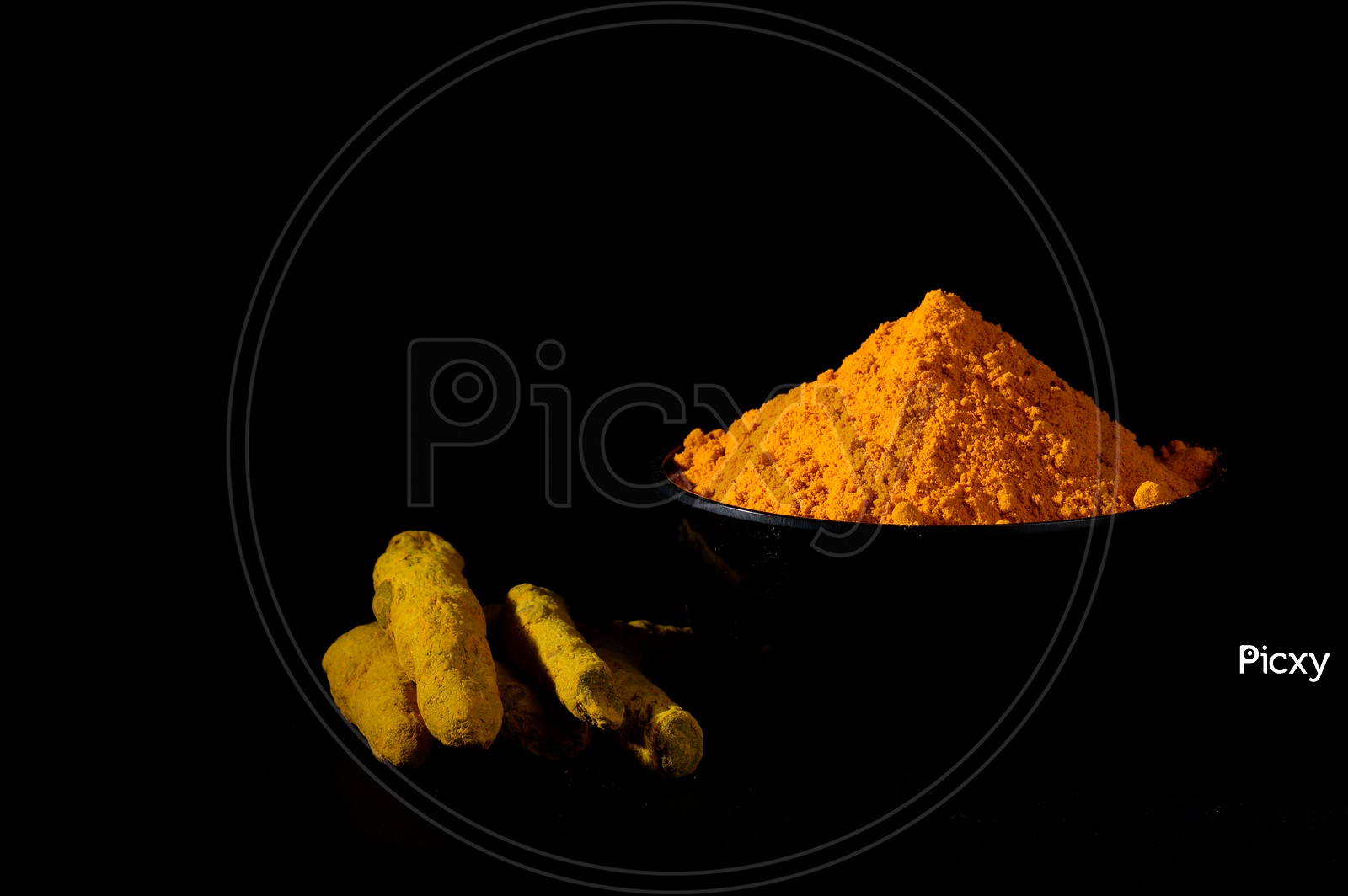 Turmeric powder and roots or barks in black bowl on black background