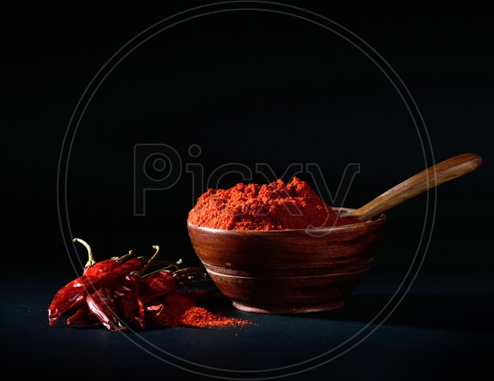 chilly powder in wooden bowl with red chilly, dried chillies on black background