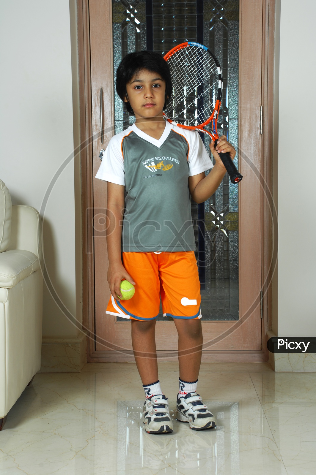 Indian boy with sportswear holding a tennis racket and ball