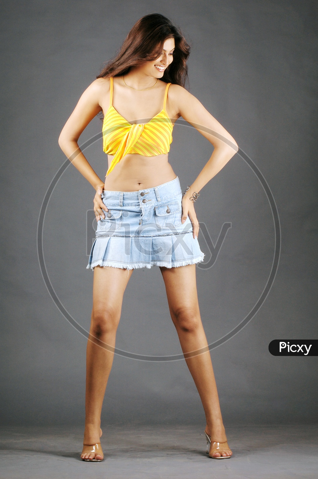 A female model with yellow crop top and frill blue mini skirt posing in a studio