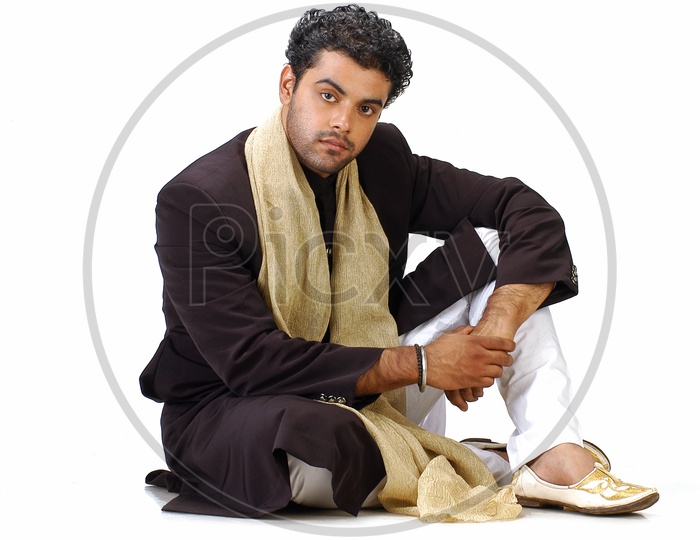 A male model sitting and posing with a Indian traditional wear - sherwani