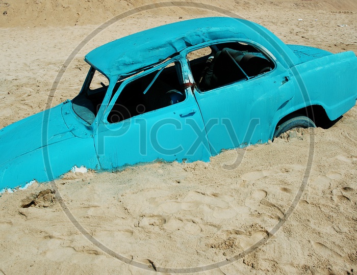 An old blue car stuck in the sand at the beach