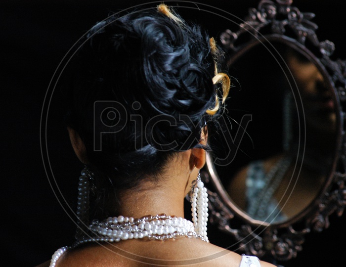An Indian Woman wearing pearl necklace looking in mirror