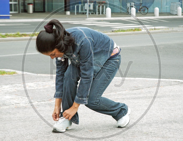 A woman wearing denims tying her shoelace