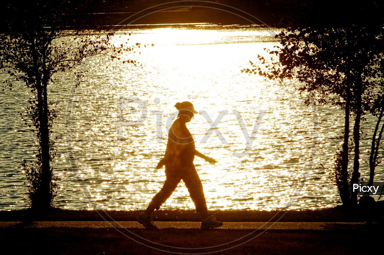 Silhouette of a woman walking beside a lake