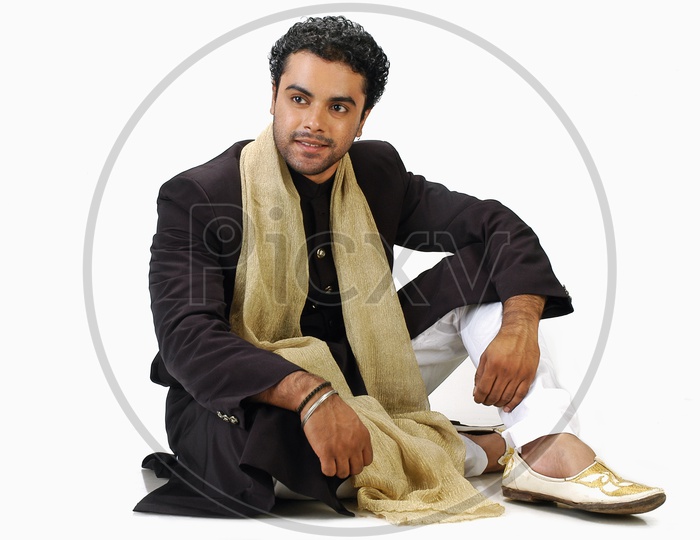 A male model sitting and posing with a Indian traditional wear - sherwani
