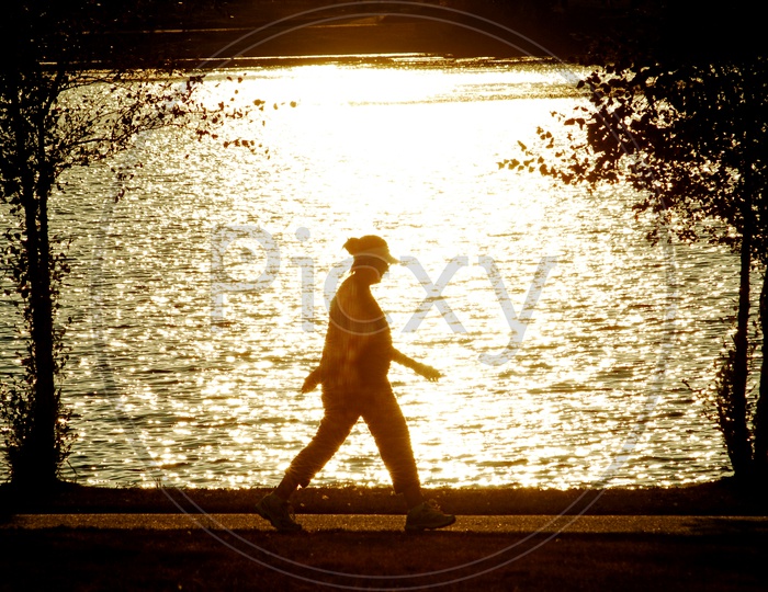 Silhouette of a woman walking beside a lake