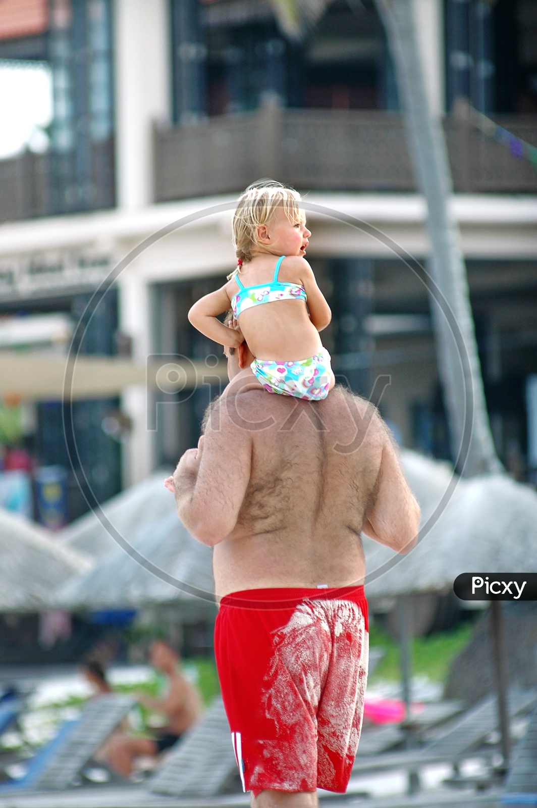 A father carrying his little girl on the shoulders in the beach wear
