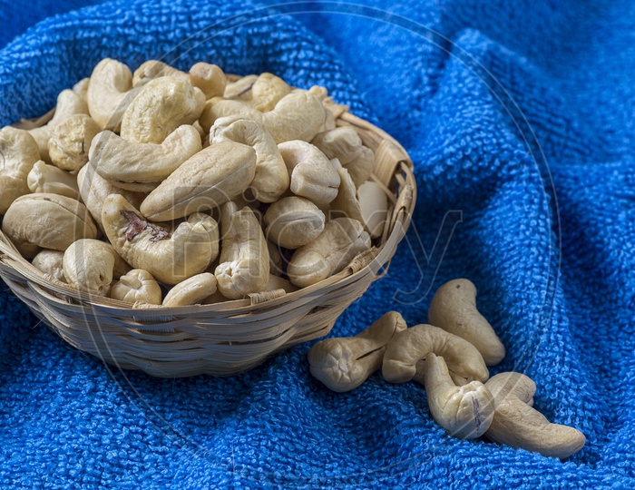 Cashew Nuts or Cashews Heap in a Wooden Weaved  Bowl On an Isolated Blue Cloth   Background