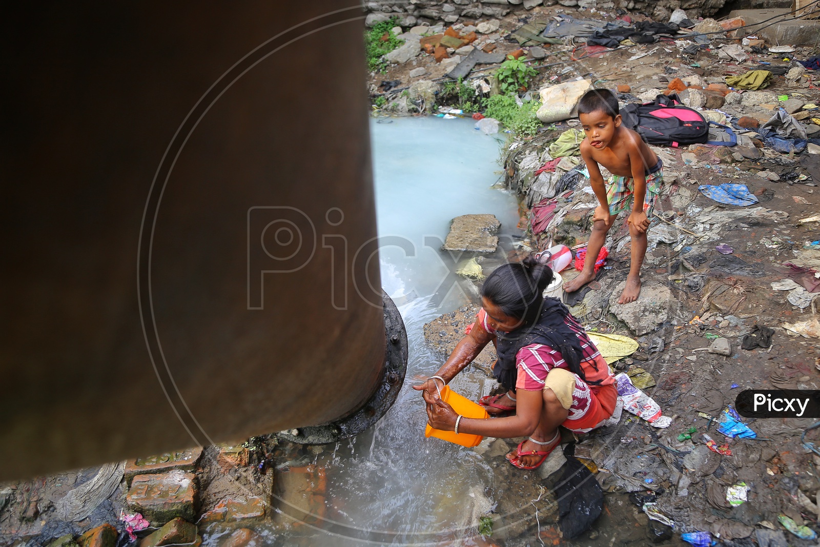 A Woman Filling The Vessel With Water Peeping Out From a Pipe Line At a Slum Area
