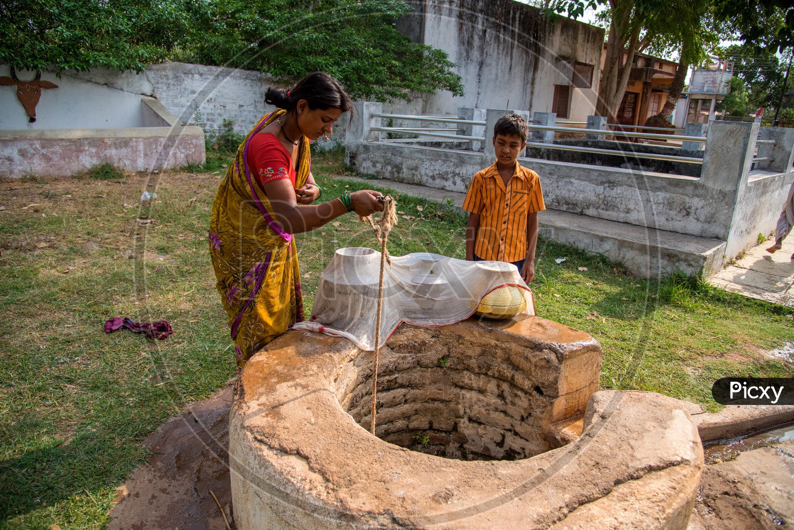 An Indian Rural Village Woman Drawing Water From a Well And Filtering Them With a White Cloth For Drinking Purpose