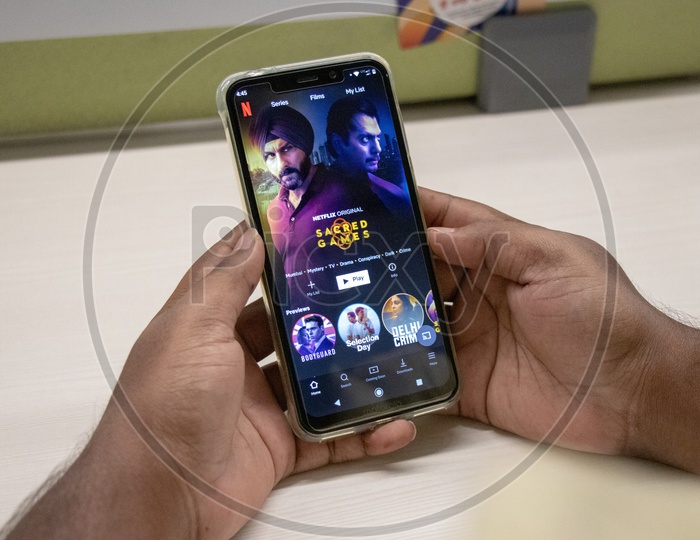 An Indian Man Watching Sacred Games 2 In His Smart Phone With a Office Desk Background