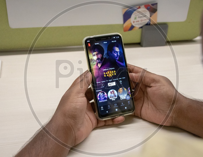 An Indian Man Watching Sacred Games 2 In His Smart Phone With a Office Desk Background