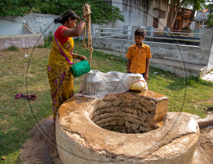 An Indian Rural Village Woman Drawing Water From a Well And Filtering Them With a White Cloth For Drinking Purpose