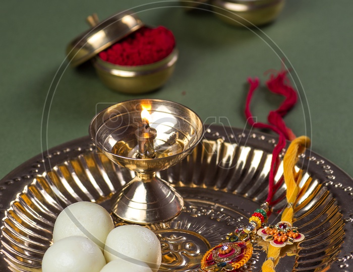 An Elegant Rakhi With a Pooja Thali With Sweet , Dia , Rice Grains And  Kumkum in That Plate