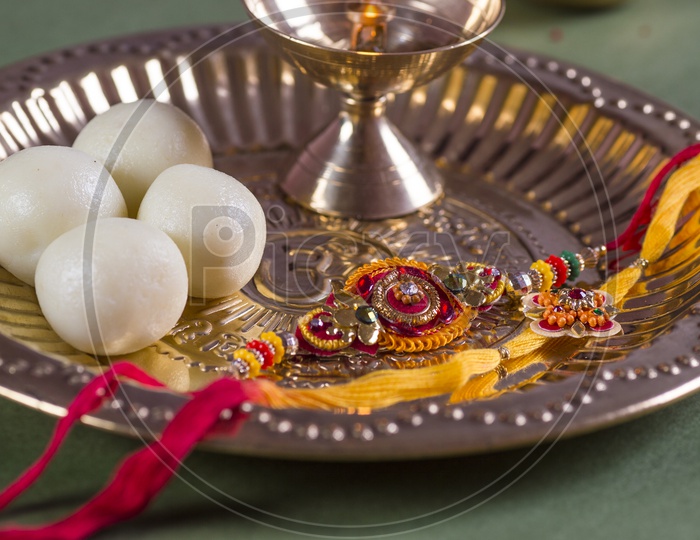 An Elegant Rakhi With a Pooja Thali With Sweet , Dia , Rice Grains And  Kumkum in That Plate