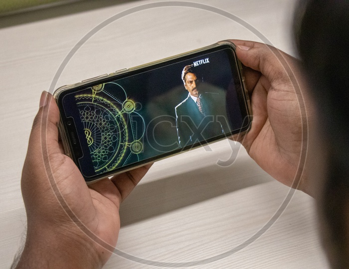 An Indian Man Watching Sacred Games 2 Trailer in  his Smart Phone  With Office Desk Background