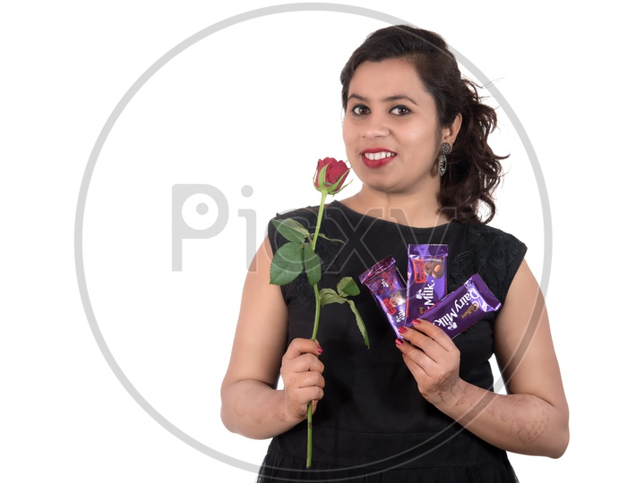 A Pretty Young Beautiful Woman Holding Diary Milk Chocolates and Rose Flower  In Hand And Smiling On an Isolated White Background