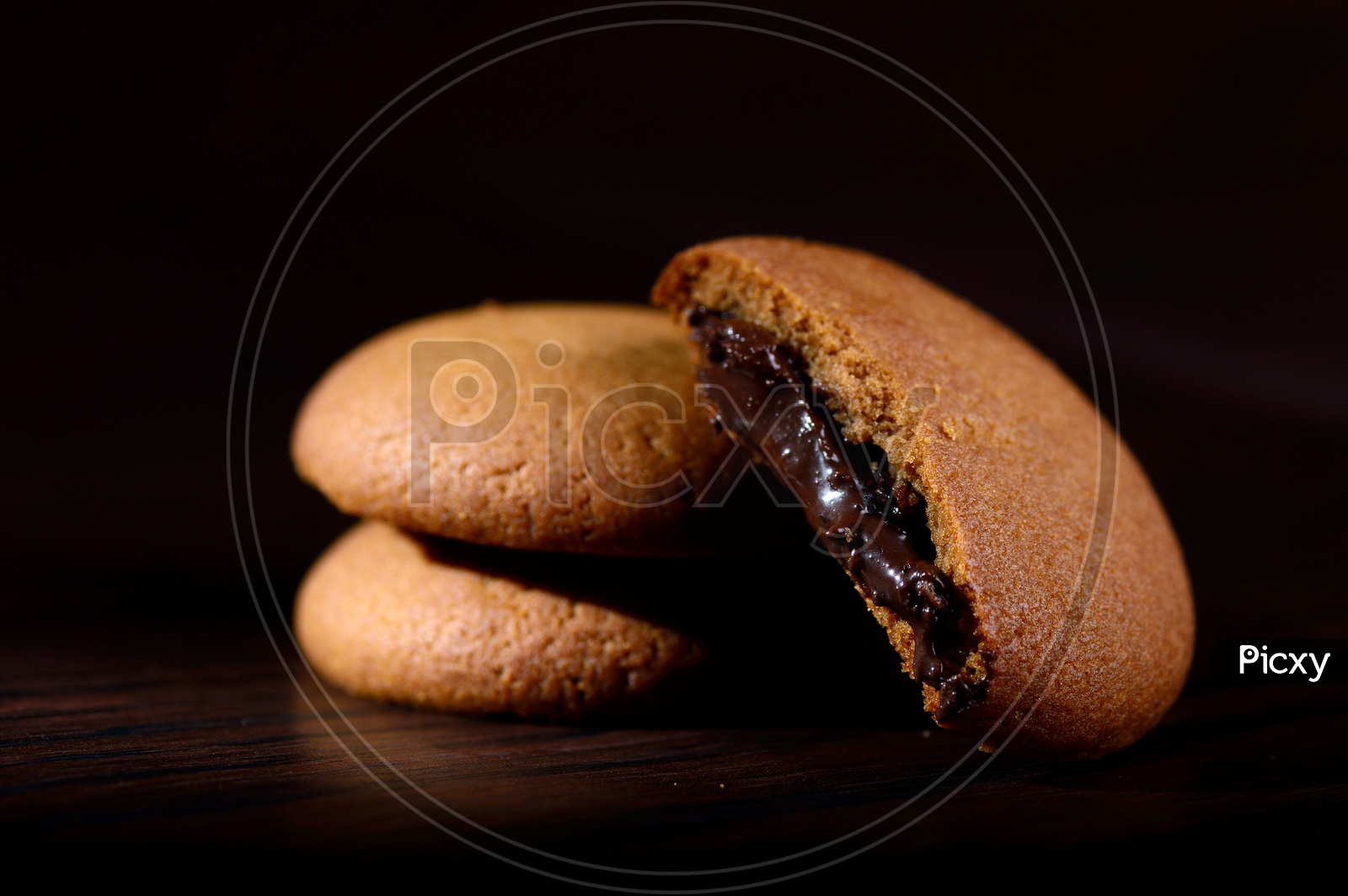 Brown chocolate biscuits with cream filling on black background.
