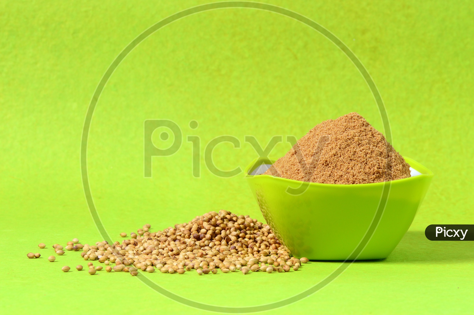 Coriander seeds and Powdered coriander in green bowl on green background.