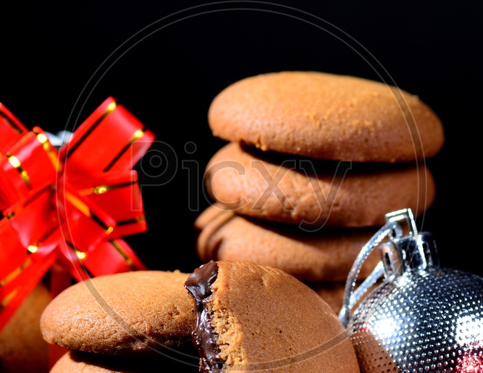BISCUITS - Stack of delicious cream biscuits filled with chocolate cream decorated with Christmas Ornaments on black background