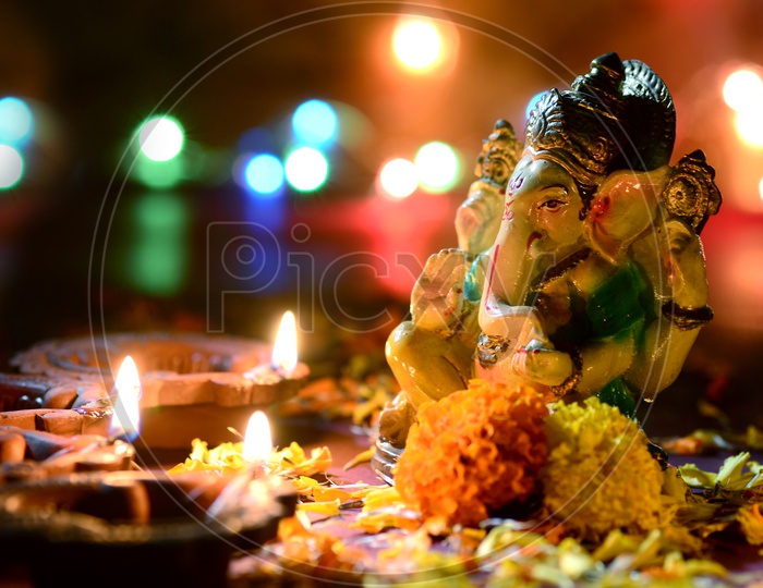 Indian Hindu God , Lord Ganesh Idol with Diwali Clay Diyas and Flowers On an Isolated Background For Ganesh or Diwali Festival Wishes or Greetings Template